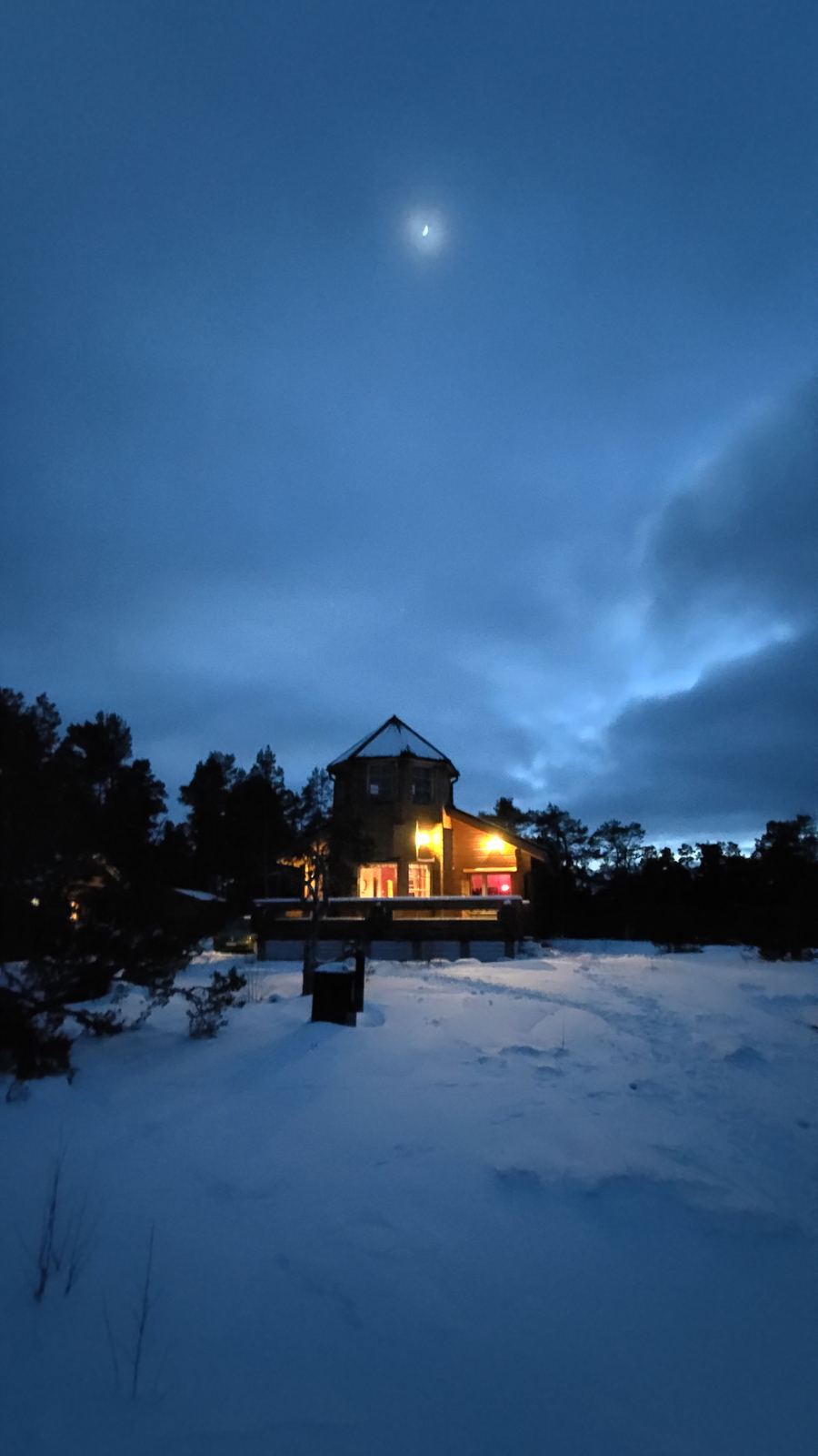 A wooden cabin glowing with warm light, surrounded by deep snow at dusk.