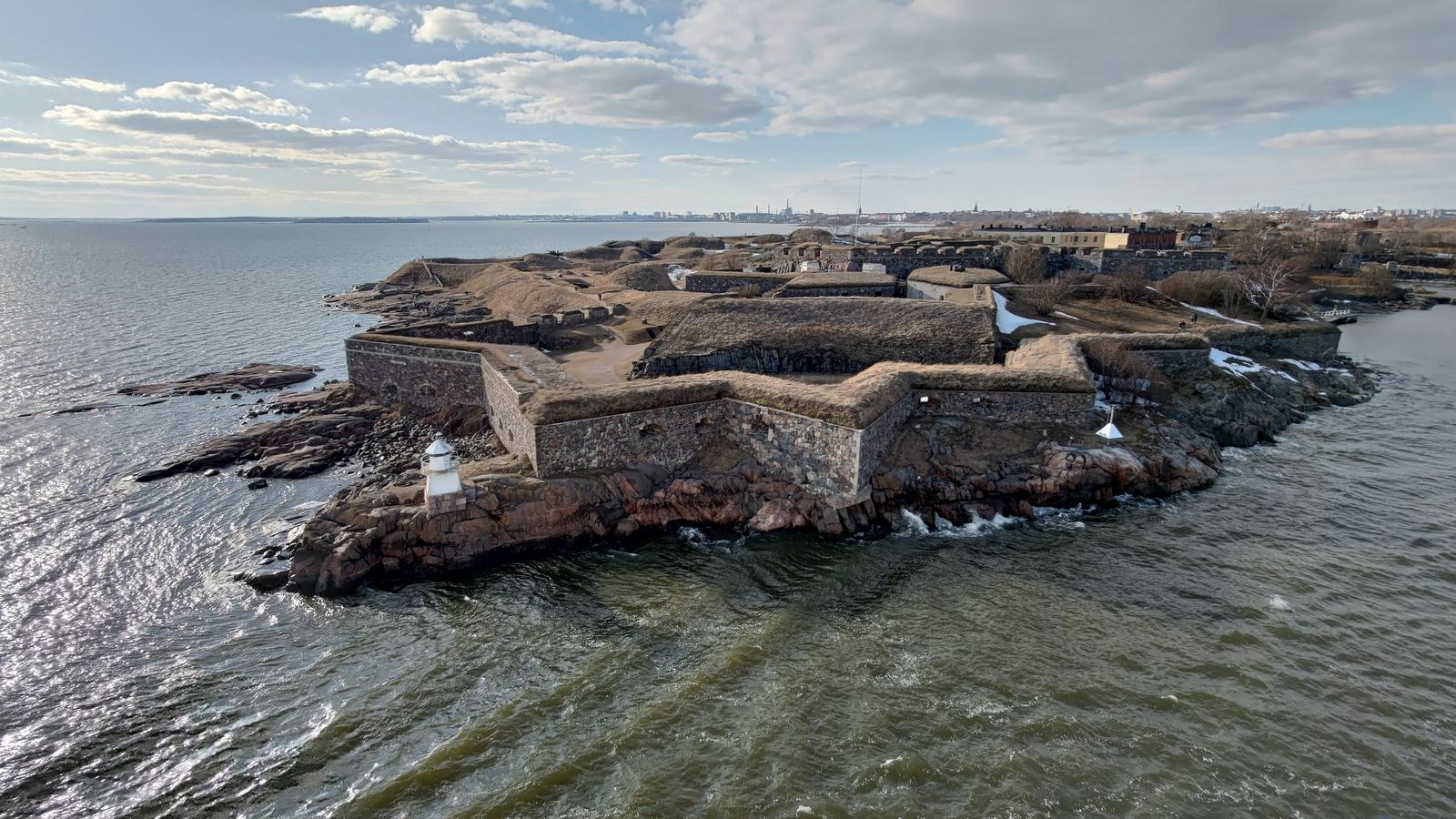 An elevated view of a wooded sea fortress with old ramparts, overlooking calm water.